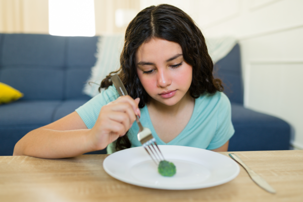 Smutná dospívající dívka s jedním kouskem brokolice na talíři – tlak diet culture, riziko porucha příjmu potravy a potřeba zdravějšího, intuitivní stravování.